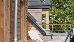 A wooden cabin with a deck, a lounge chair, and a small table.