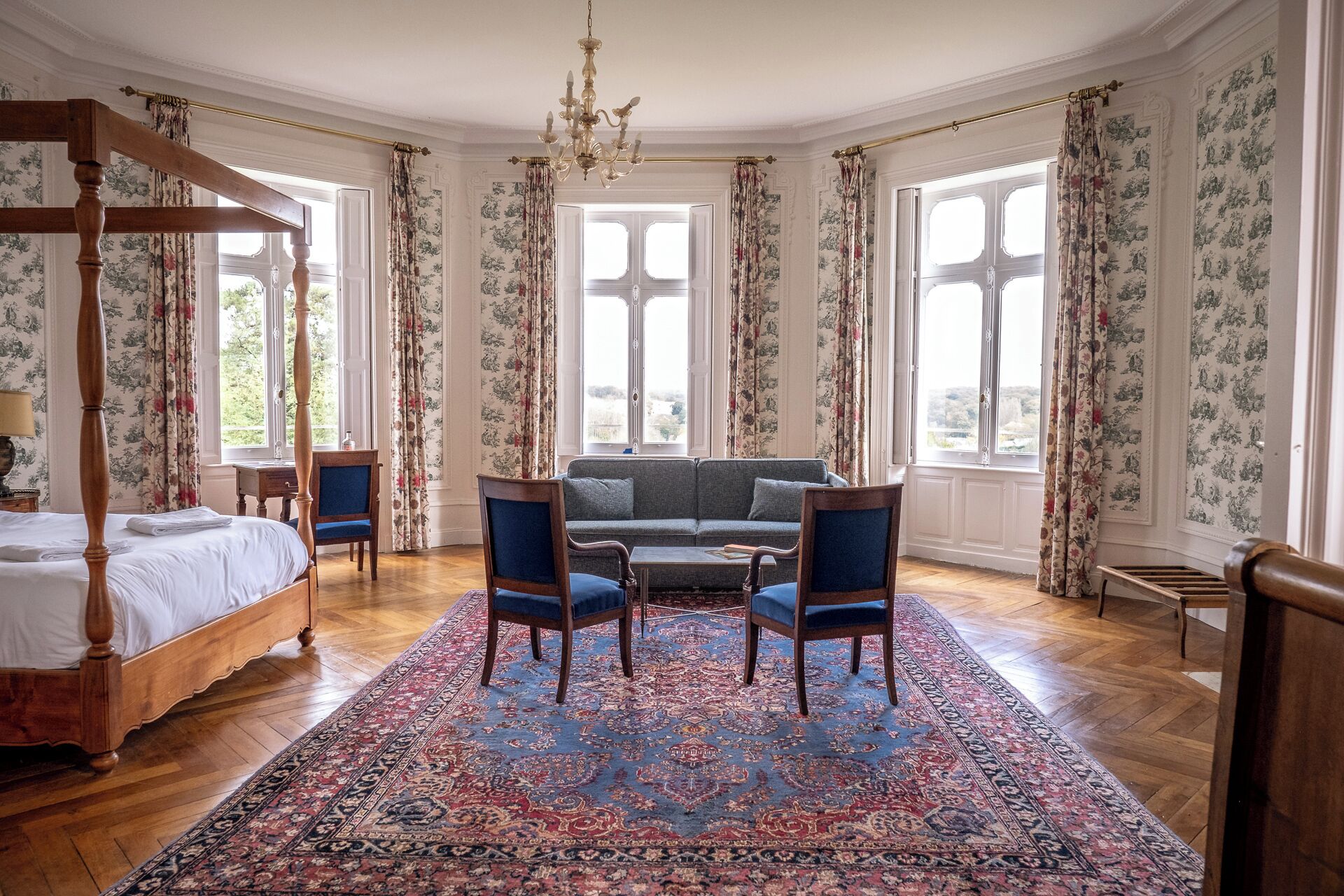 Una habitación amplia con una cama con dosel, un sofá, dos sillones y una alfombra estampada.
