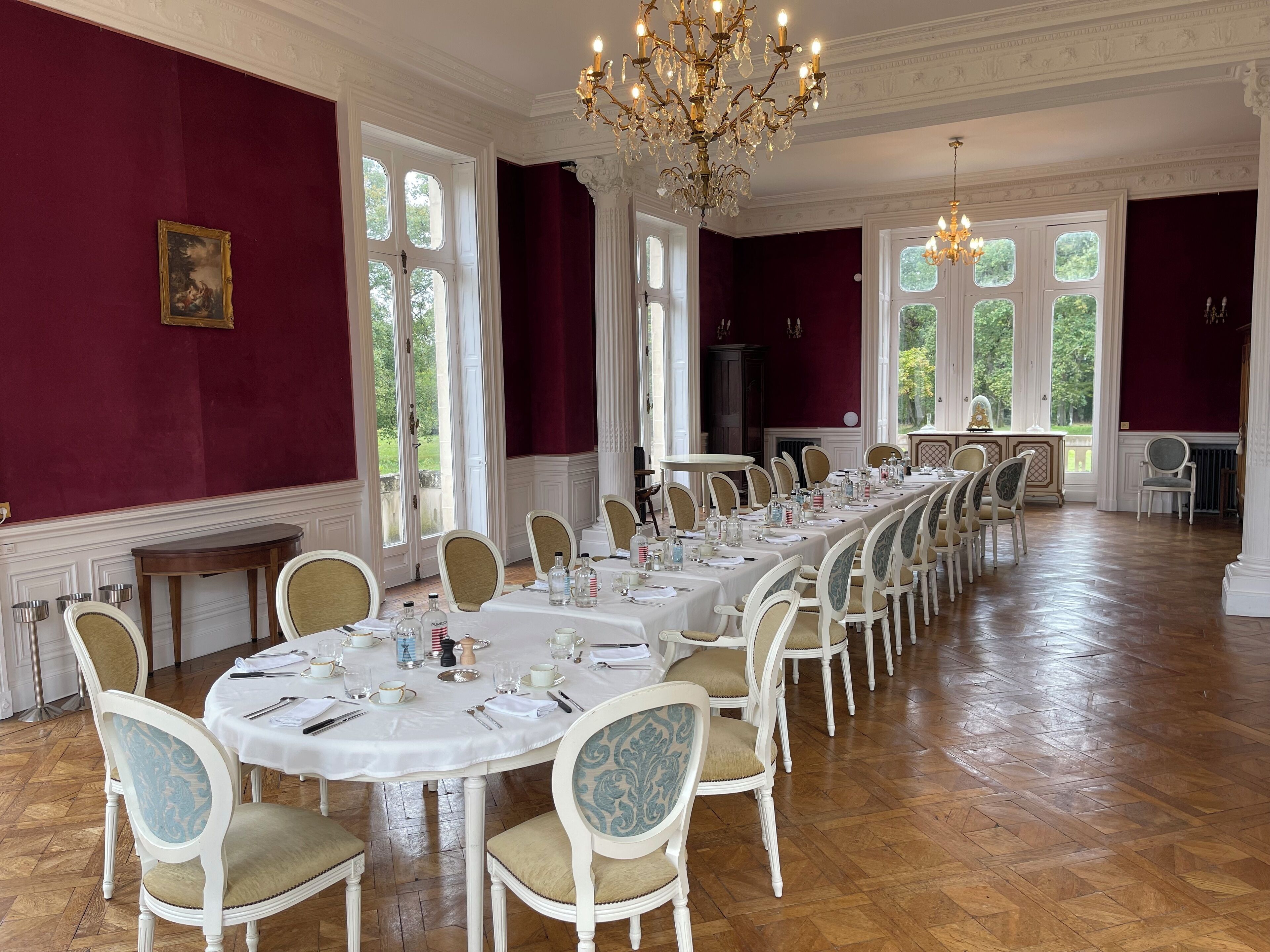 A formal dining room with a long table set for a meal, surrounded by chairs with cushioned seats.