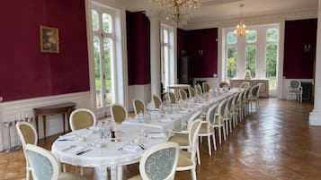 A formal dining room with a long table set for a meal, surrounded by chairs with cushioned seats.