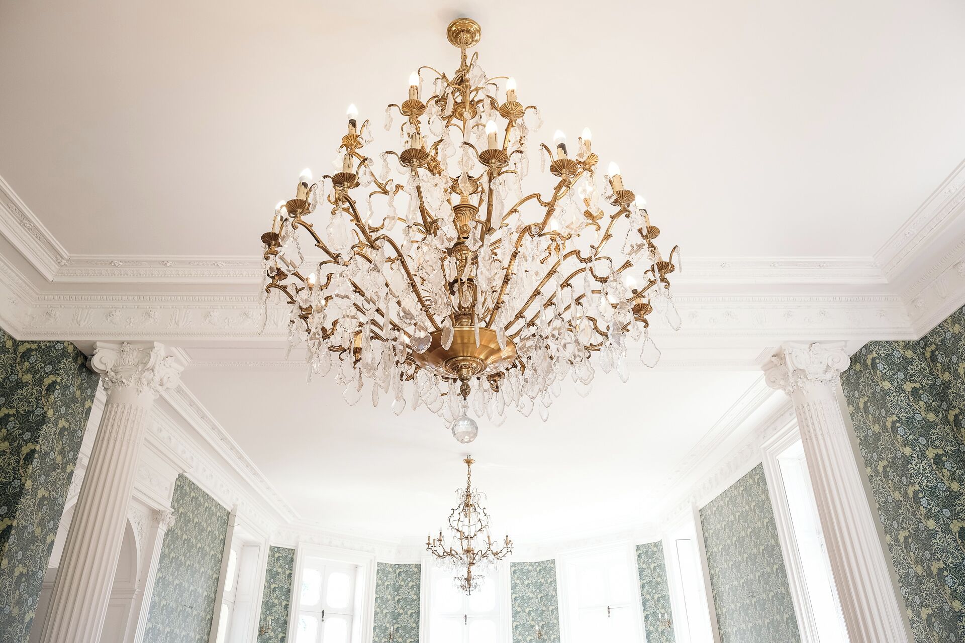 A grand chandelier in a room with ornate columns and patterned wallpaper.