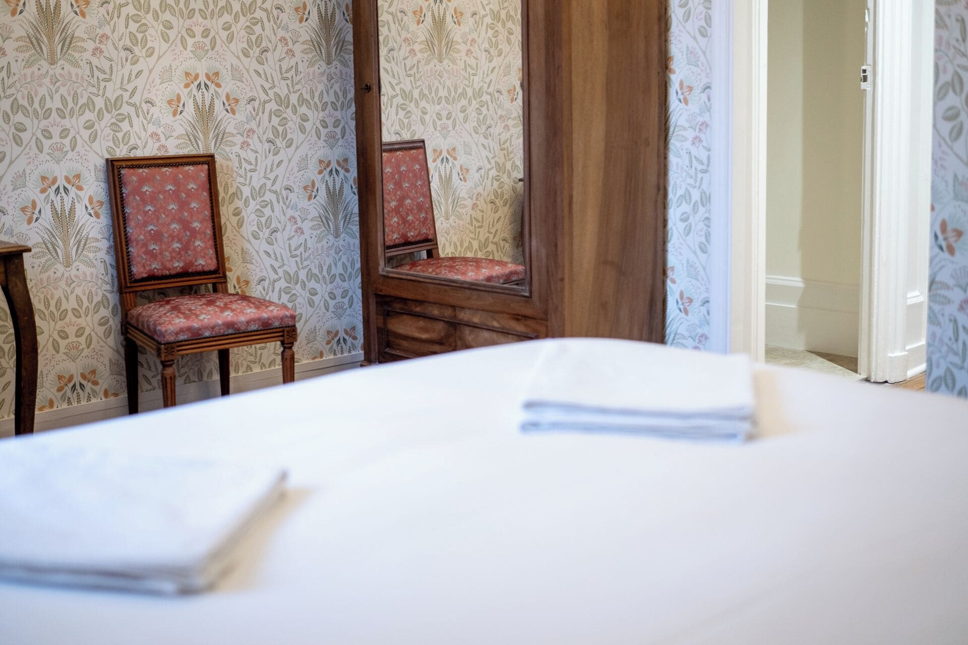 Una habitación de hotel con una cama, dos sillas, un espejo y una puerta.