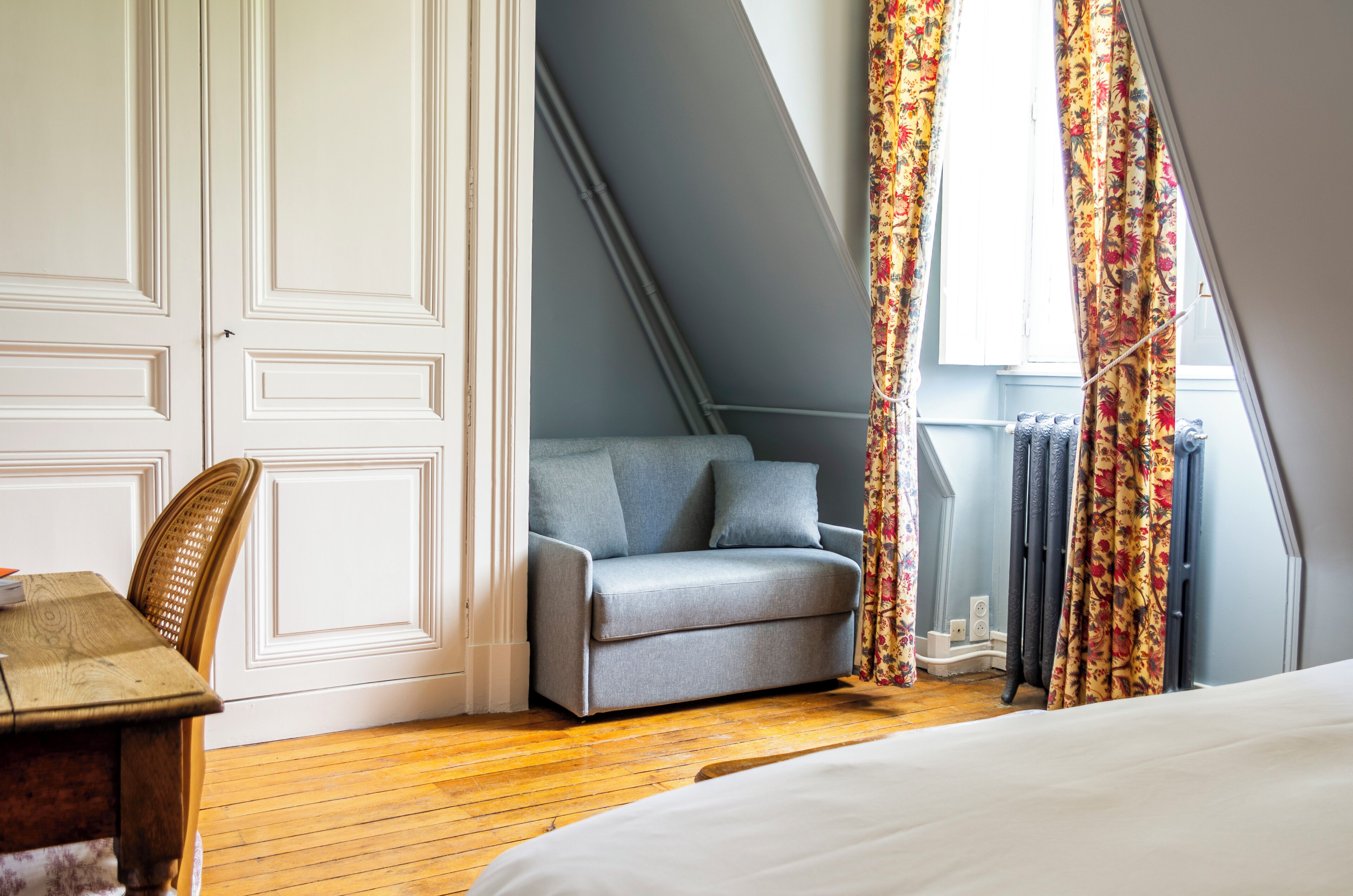 A bedroom with a bed, a grey sofa, a wooden table, and a chair.