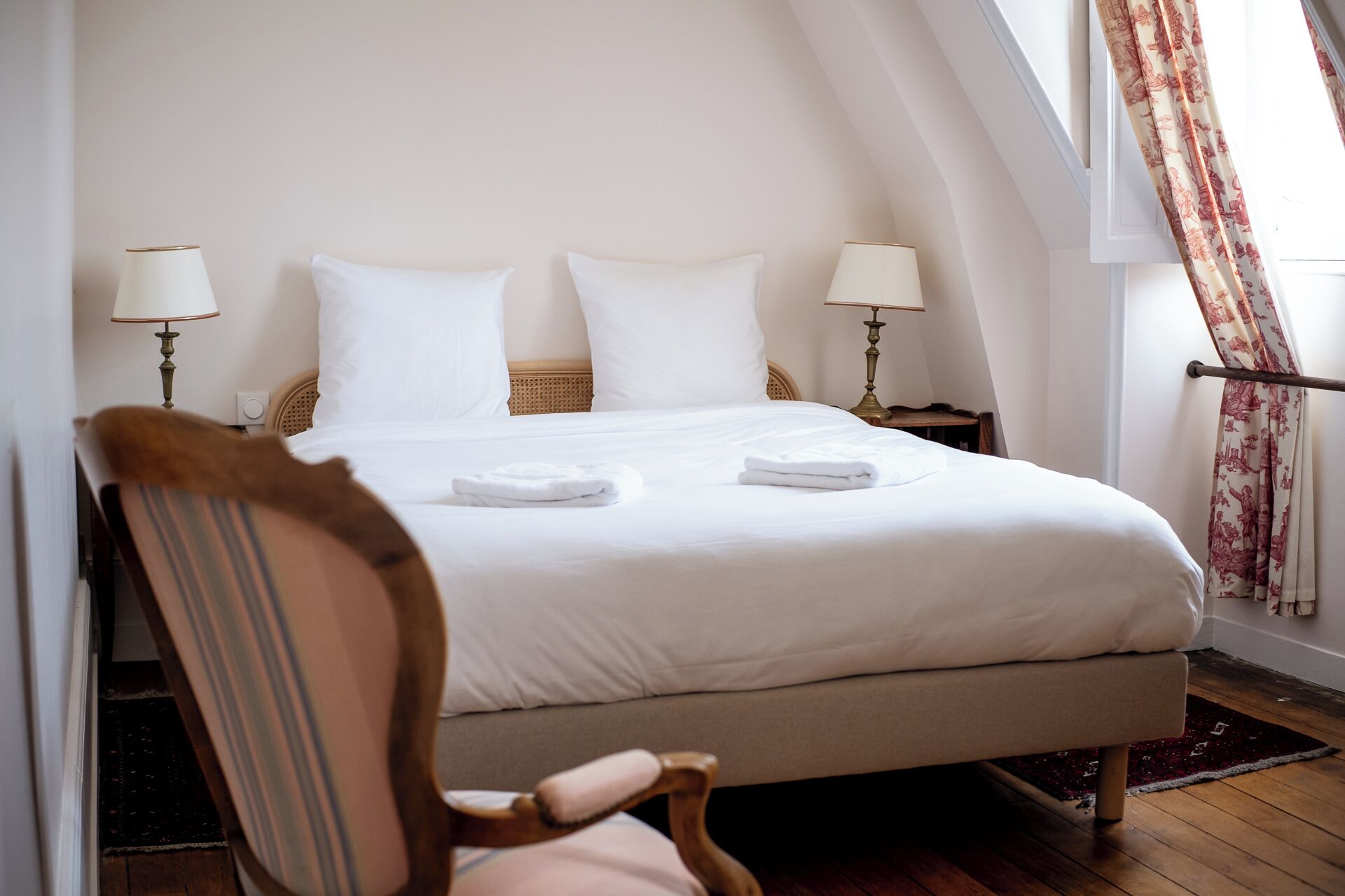 A neatly made bed with white linens and two pillows, flanked by two bedside lamps.