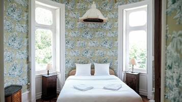 Une chambre avec un grand lit, deux tables de chevet, un luminaire suspendu et une fenêtre donnant sur un paysage verdoyant.