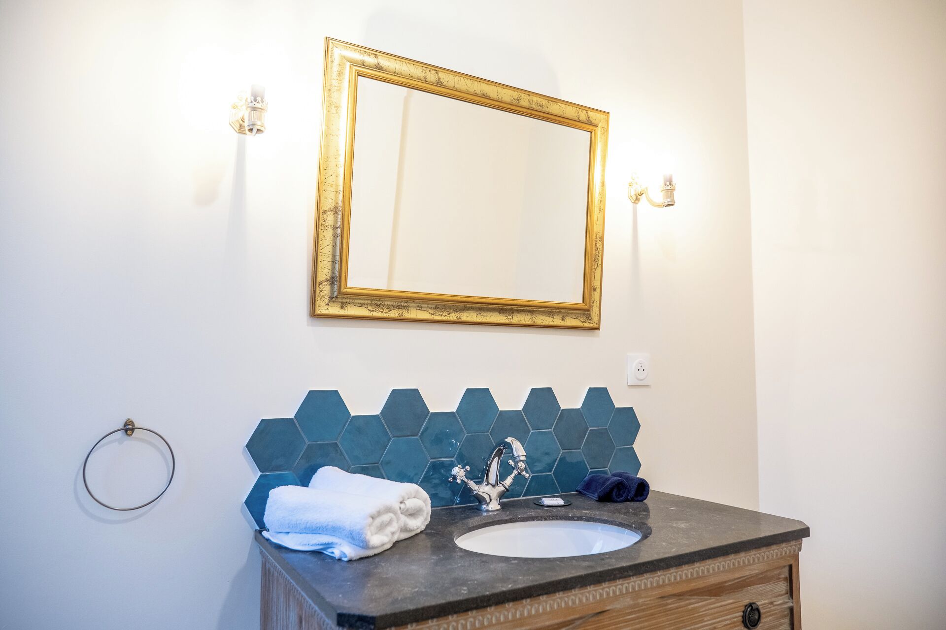 A bathroom with a gold-framed mirror, a sink with a hexagonal tile backsplash, and a towel rack.