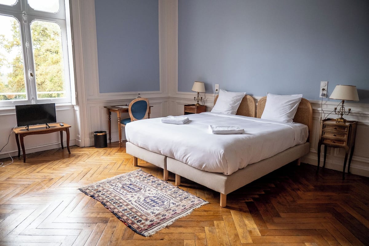 Een slaapkamer met een groot bed, een televisie op een houten tafeltje en een raam met uitzicht op bomen.