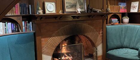 A cozy room with a fireplace, two teal armchairs, a coffee table, and a bookshelf with books and decorative items.