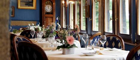 Un espace repas avec des tables mises pour le repas, agrémenté de compositions florales et d’une horloge au mur.