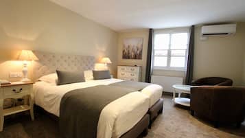 Habitación de hotel con una cama grande, mesitas de noche con lámparas, una pequeña mesa redonda, un sillón marrón y una ventana con cortinas.