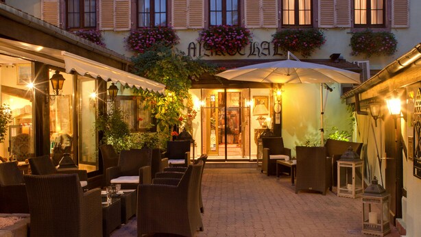 Un edificio tradicional europeo con un patio central, que cuenta con un restaurante con mesas al aire libre y un letrero que dice "ALTERNATE".