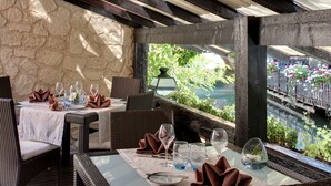 Un comedor con mobiliario de mimbre, paredes de piedra y vista a un jardín por una ventana.