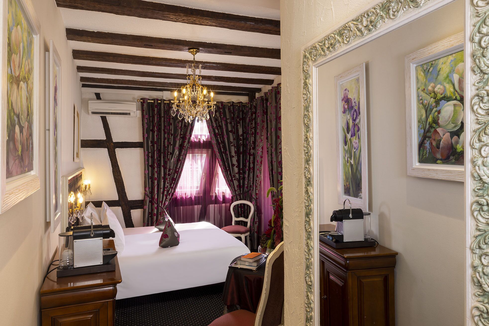 Una camera d'albergo con un letto, una scrivania con una lampada, una sedia, un comò e un lampadario.