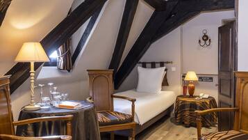 A cozy room with a bed, a table with a lamp, a chair, and a small table with a lamp. There is a sign on the wall that reads "SORTIE DE SECOURS".