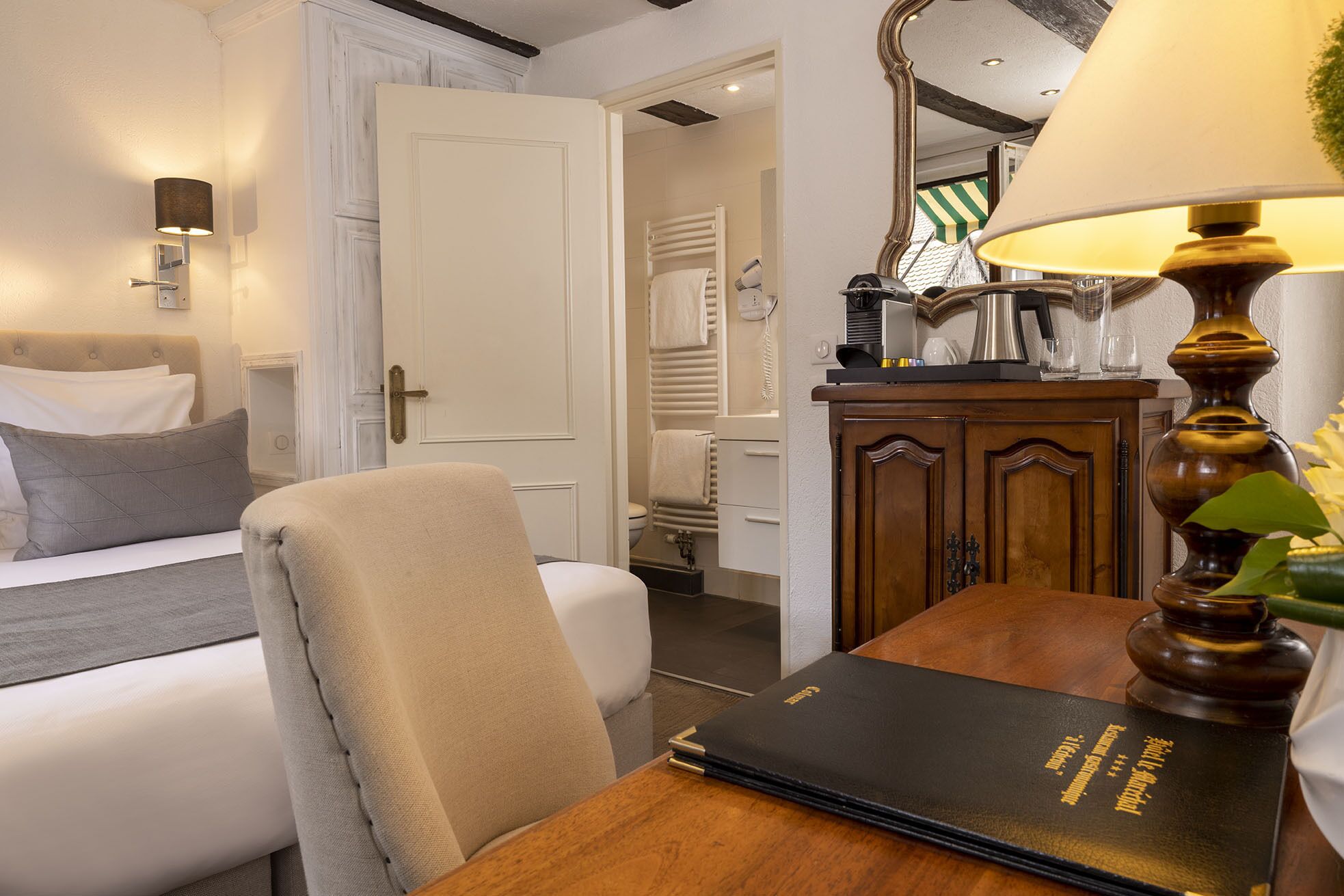 Una camera d'albergo con un letto, una sedia, una scrivania con un libro, una lampada e un armadio.