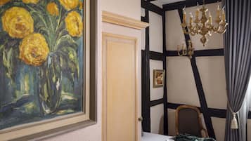 A room with a large painting of yellow flowers, a wooden door, a chandelier, and a bed with a blanket.