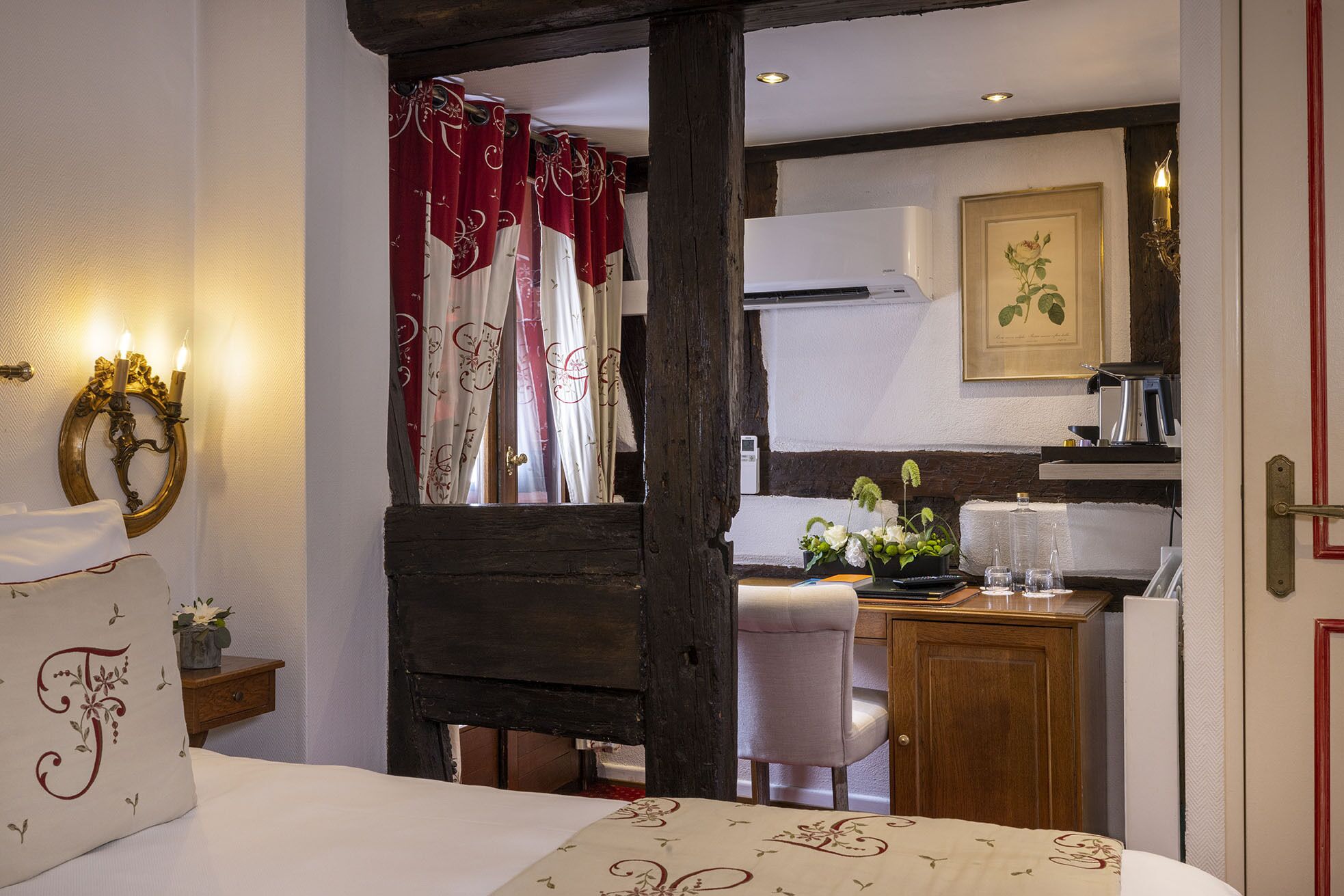 A bedroom with a bed, a nightstand, a desk, a chair, a mirror, and a window with curtains.