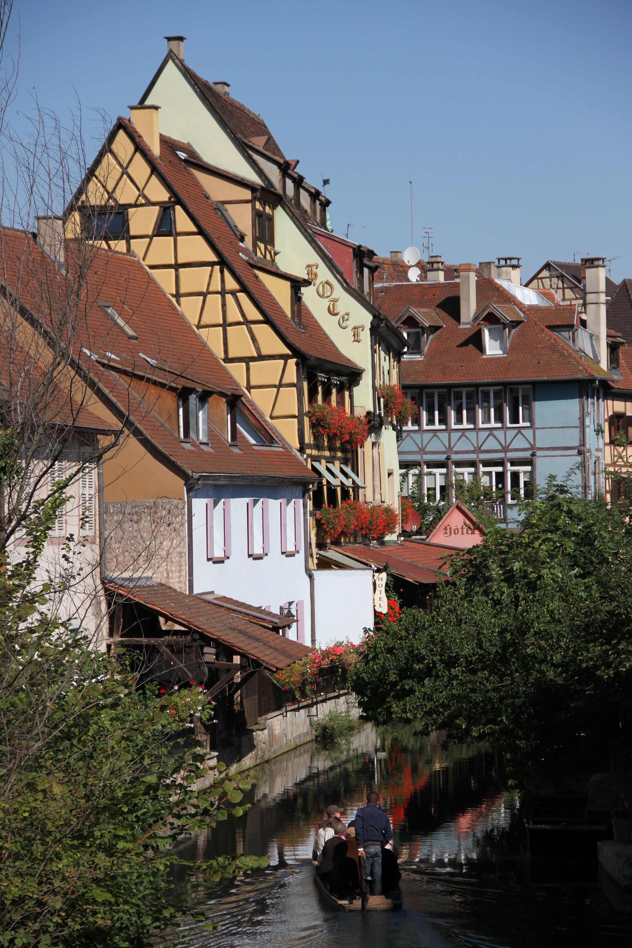 Un étroit canal bordé de bâtiments traditionnels à colombages, dont l’un porte une enseigne visible.