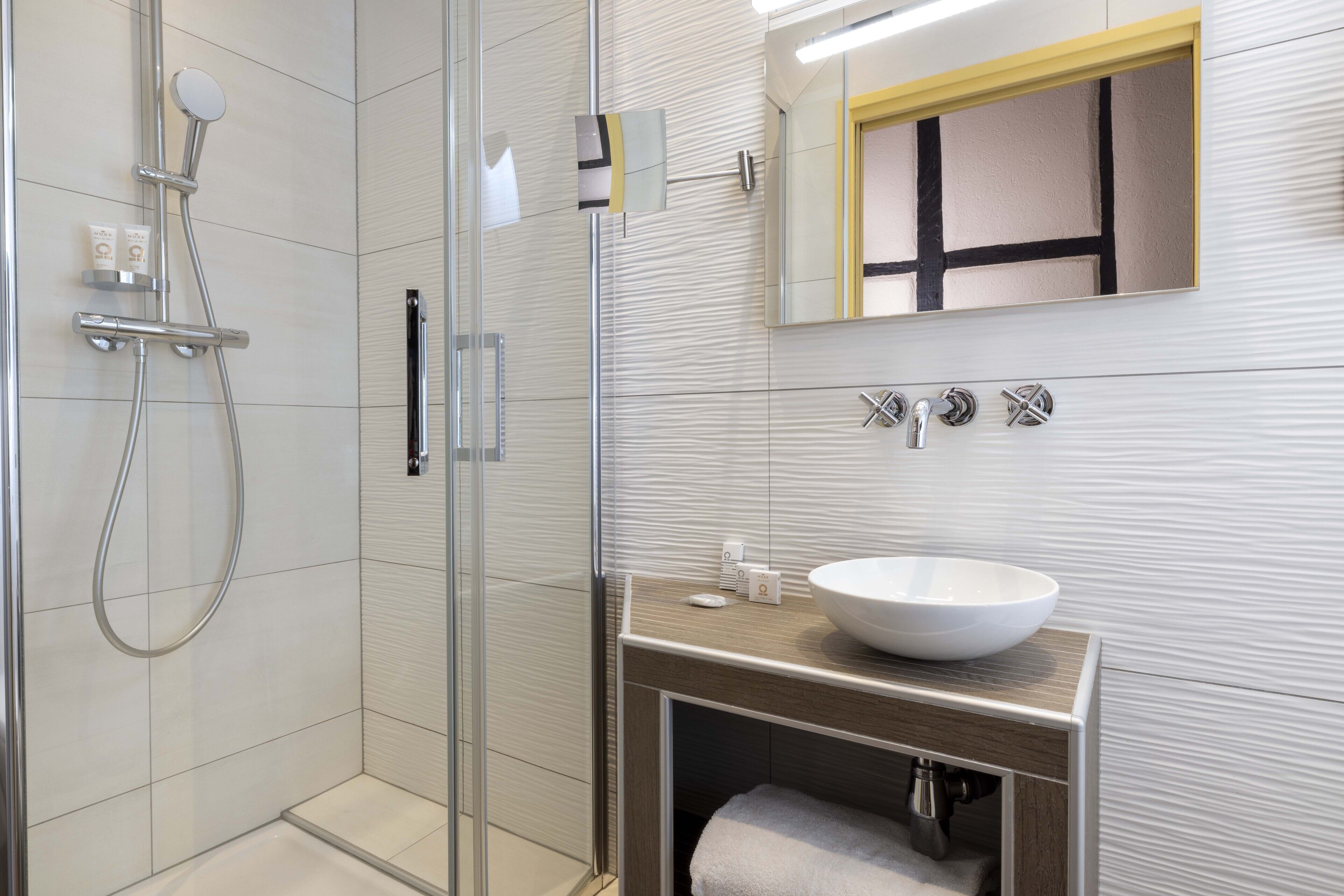 Un baño moderno con ducha de vidrio, un lavamanos grande blanco y un mueble de tocador de madera.