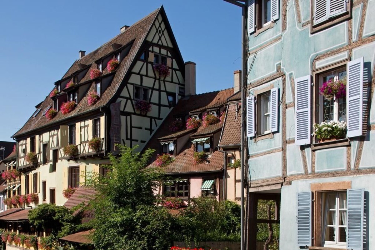 Una hilera de edificios europeos tradicionales con entramado de madera y macetas con flores en los alféizares.