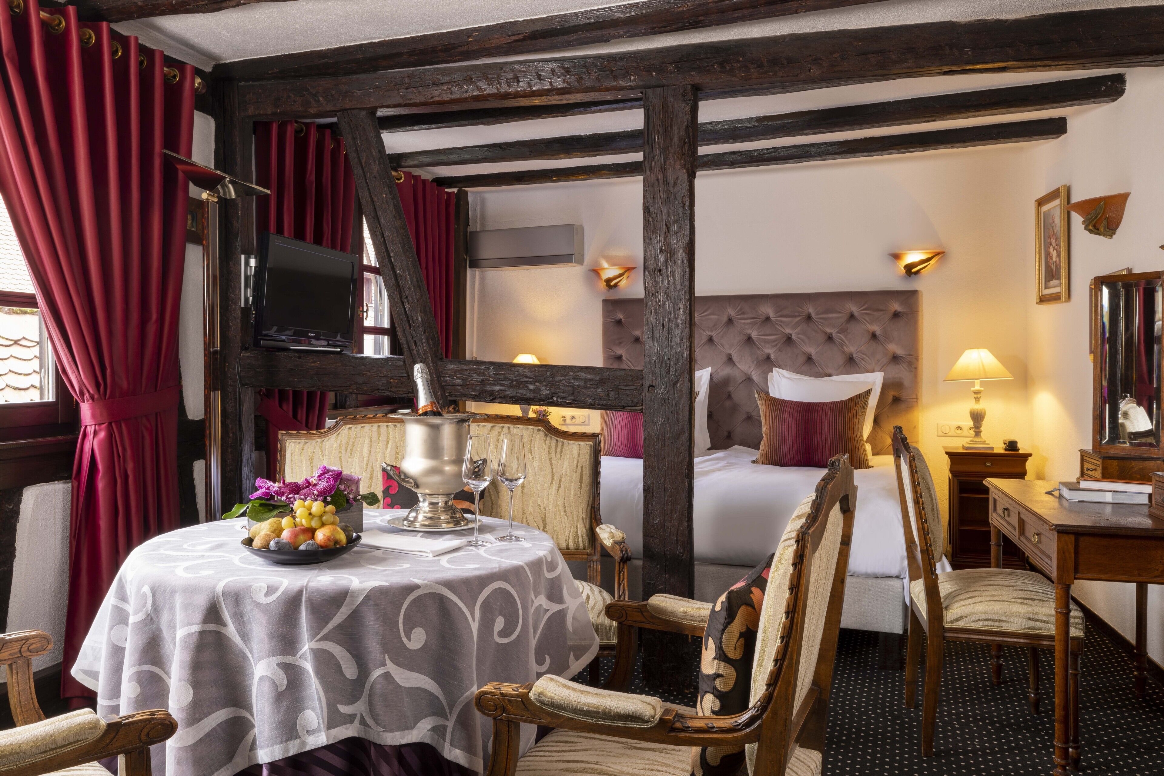 Habitación de hotel con cama, una mesa con frutero, una silla, escritorio de madera y televisión.