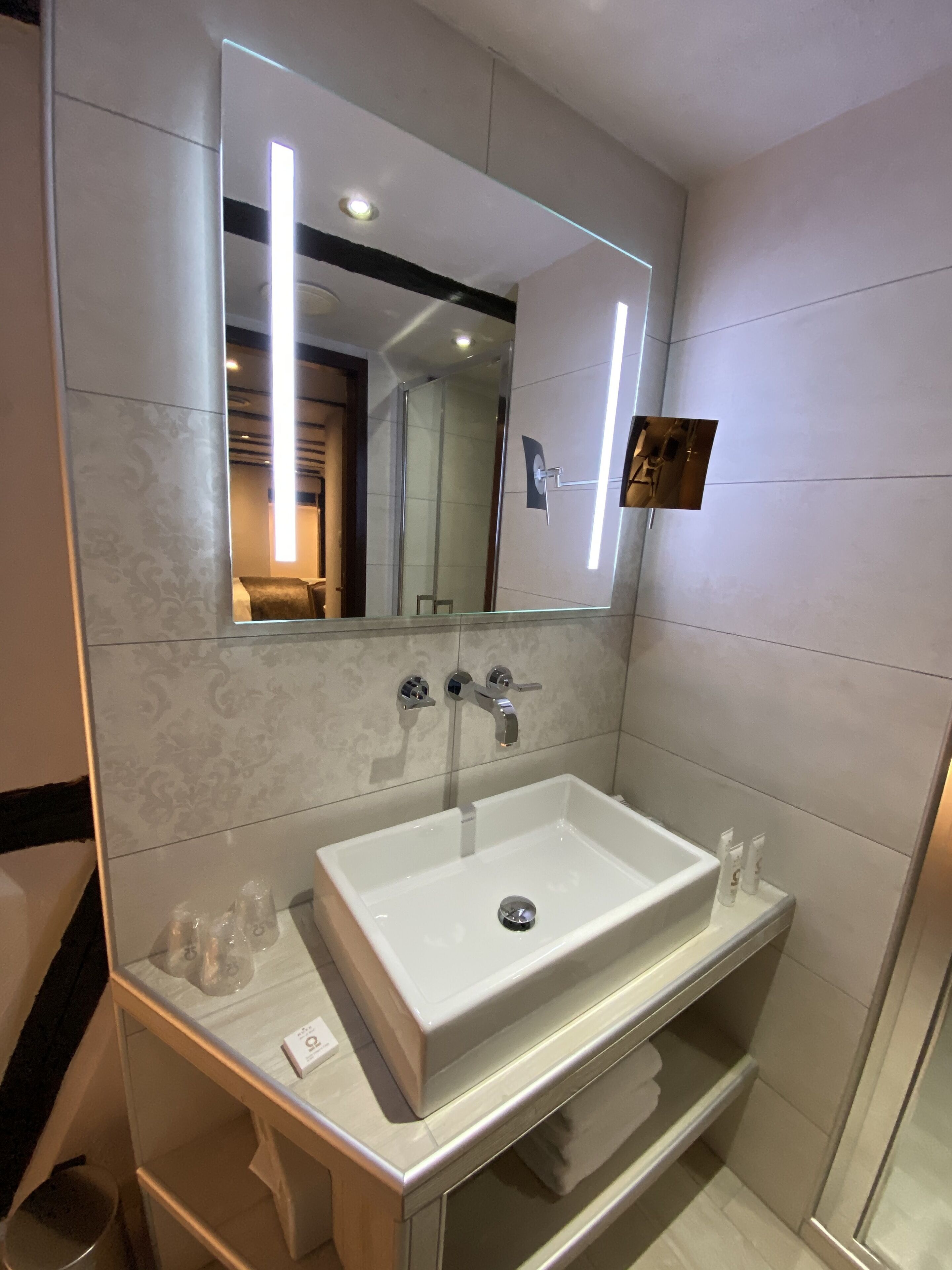 A modern bathroom with a large mirror, a white sink, and a glass shower enclosure.