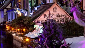 Un hotel con fachada de estilo europeo tradicional, un cartel anunciando el restaurante y una figura decorativa de ciervo.