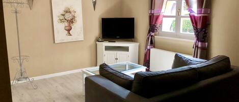 A living room with a sofa, a TV on a cabinet, a painting on the wall, and a window with curtains.
