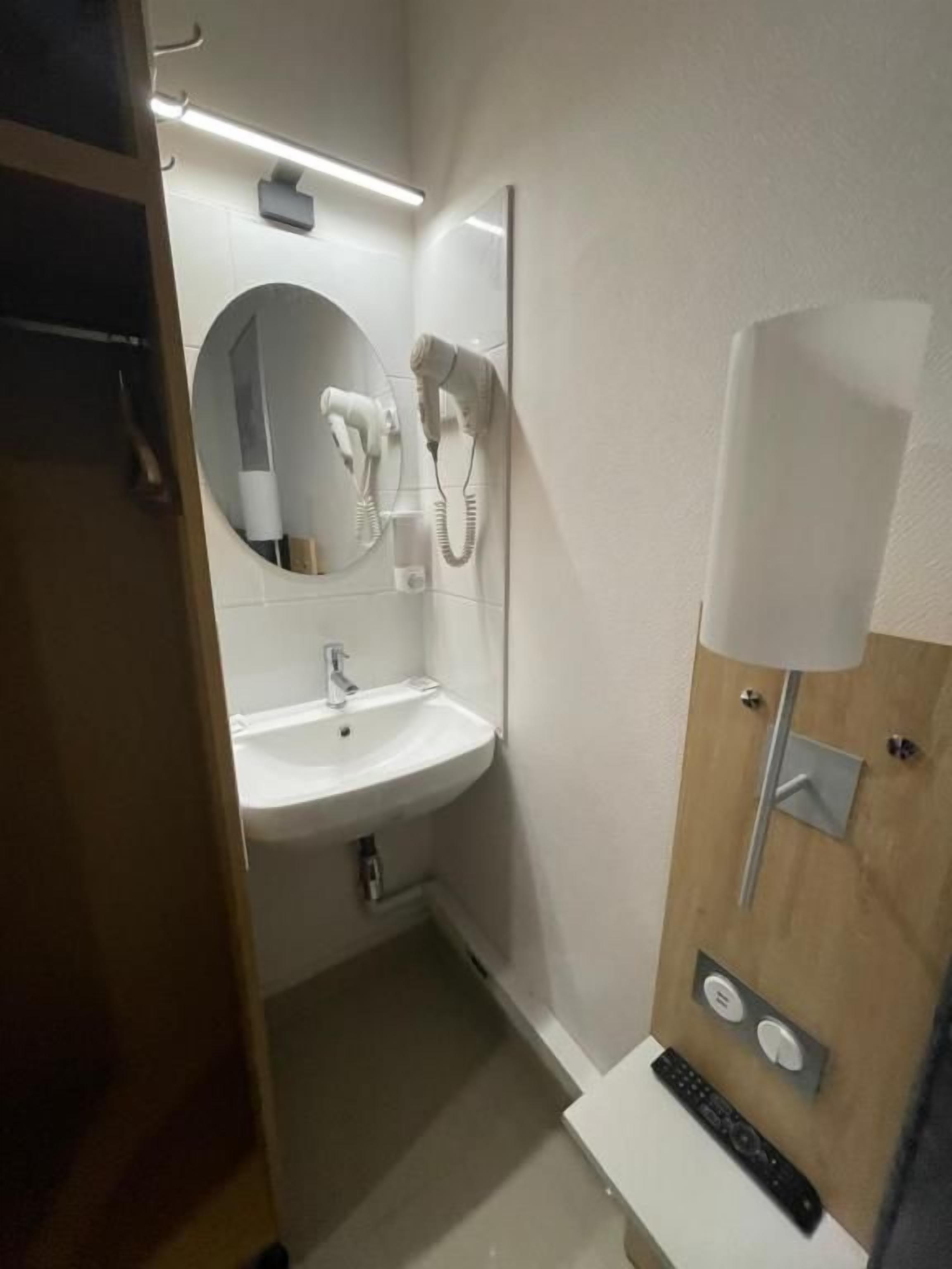 Une salle de bain équipée d’un lavabo, d’un miroir, d’un sèche-cheveux et d’un porte-serviettes.