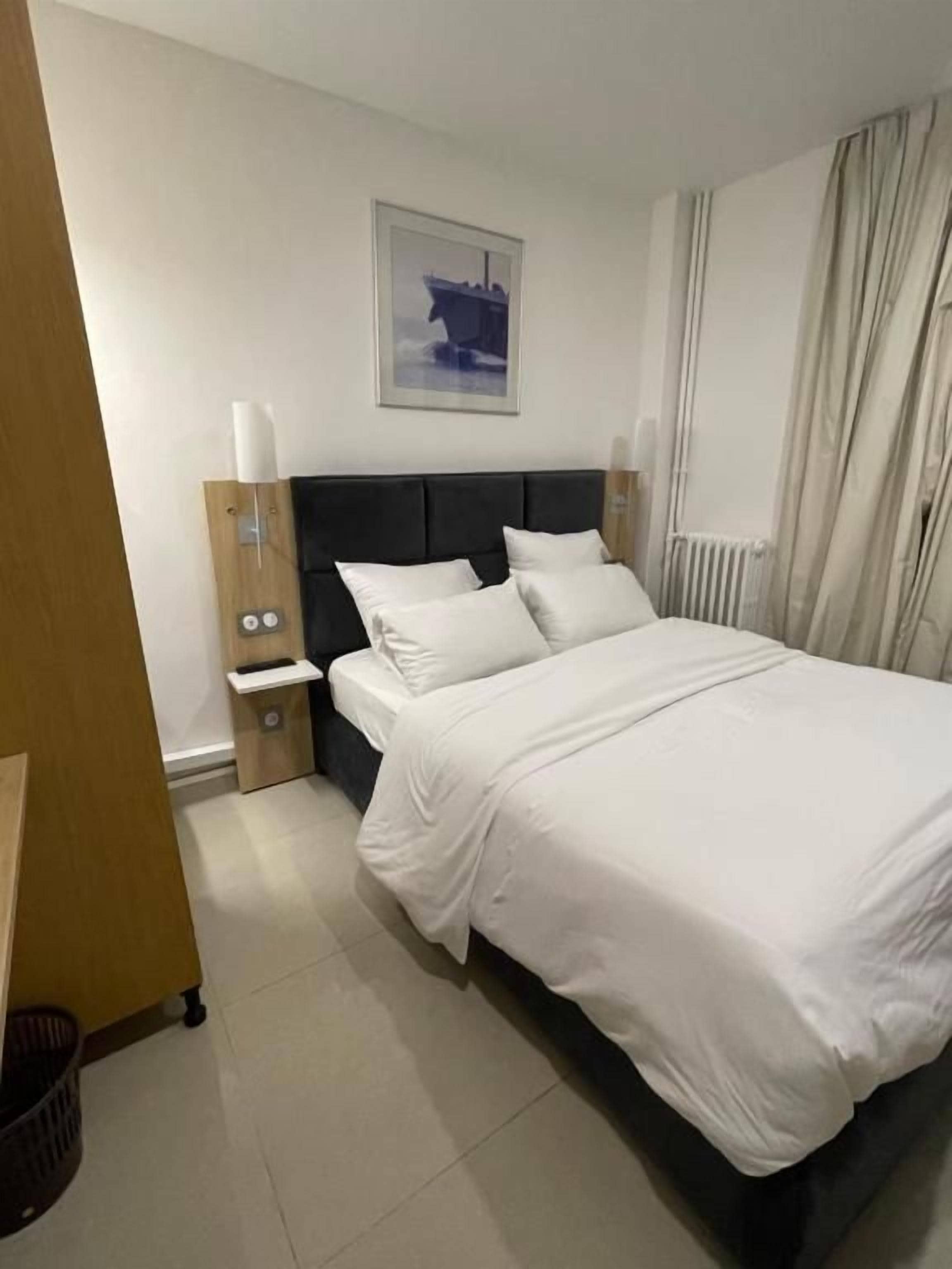 A hotel room with a bed, nightstands, a wall-mounted picture, and a window with curtains.