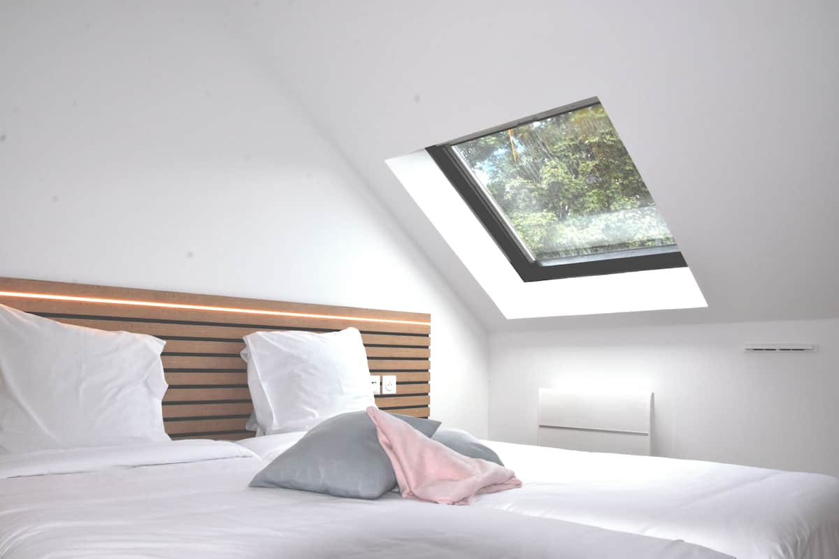 A modern bedroom with a skylight, a wooden headboard, and a bed with white and gray bedding.