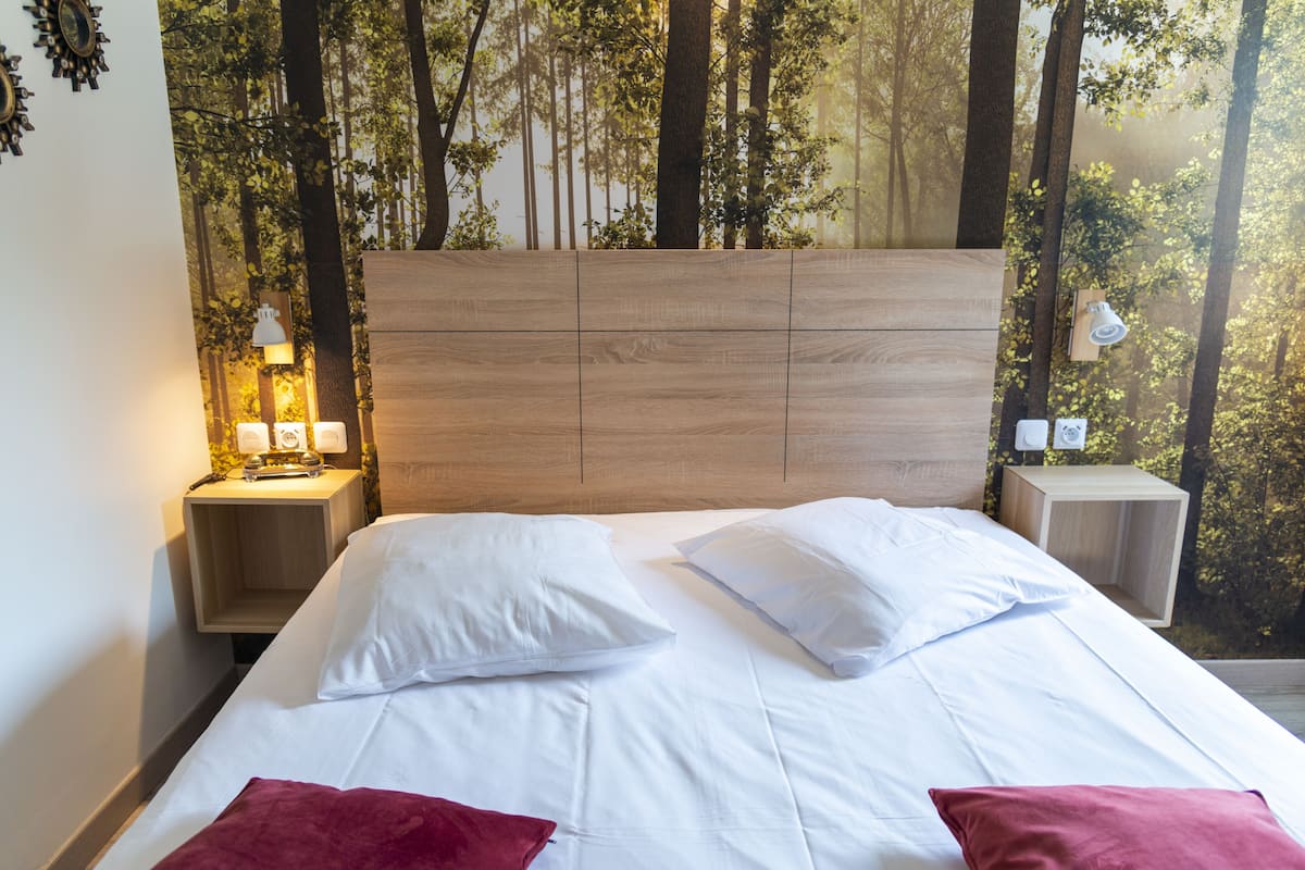 A neatly made bed with white bedding and two red pillows, a wooden headboard, and nightstands with lamps.