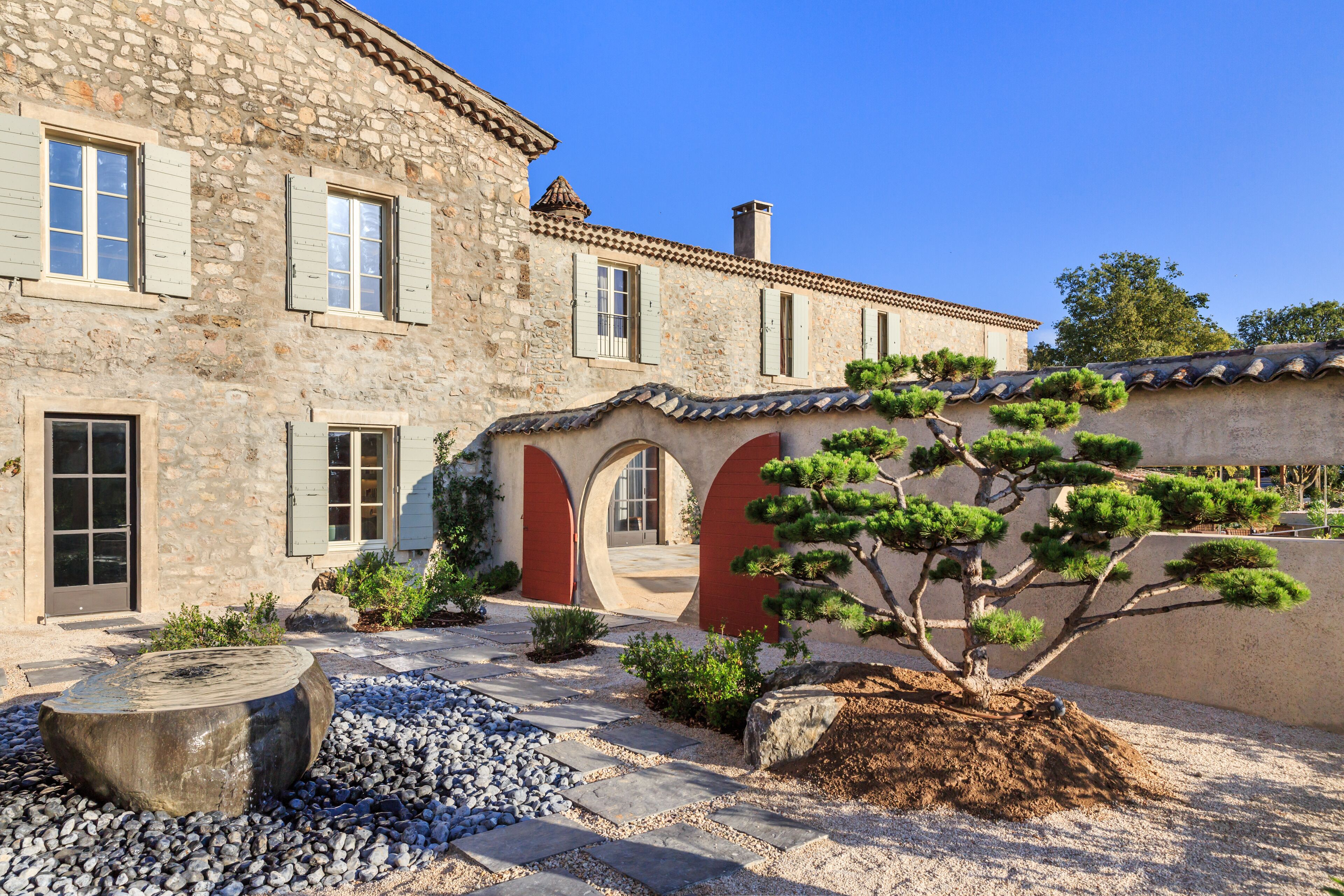 A stone building with a courtyard, featuring a large tree and a stone bench.