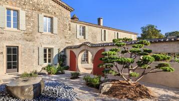 A stone building with a courtyard, featuring a large tree and a stone bench.