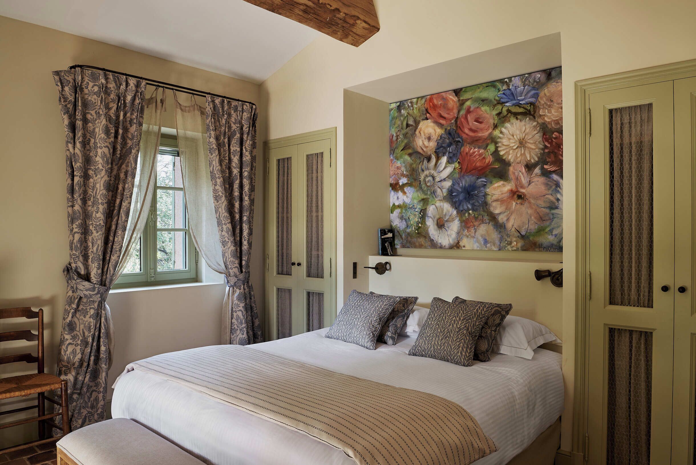 A bedroom with a bed, curtains, a painting, and a door.