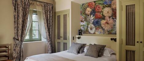 A bedroom with a bed, curtains, a painting, and a door.