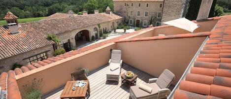 Une terrasse sur le toit, avec des sièges en plein air, une table et une vue sur un bâtiment historique et des collines boisées.