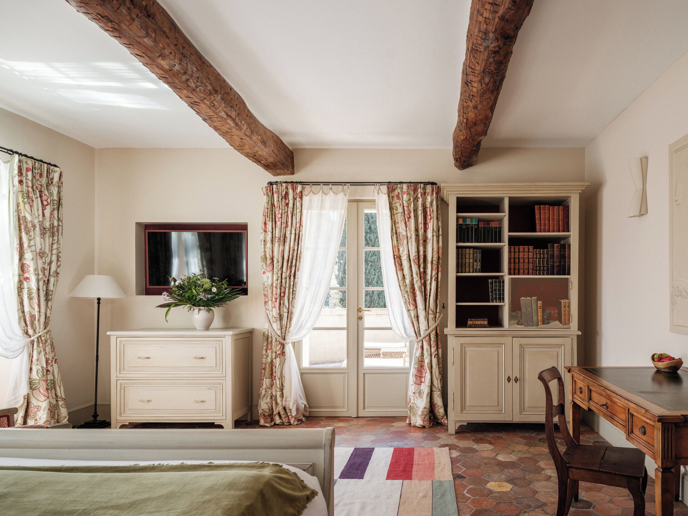 Une chambre à coucher avec un lit, une commode, un bureau, une bibliothèque et une fenêtre avec des rideaux.