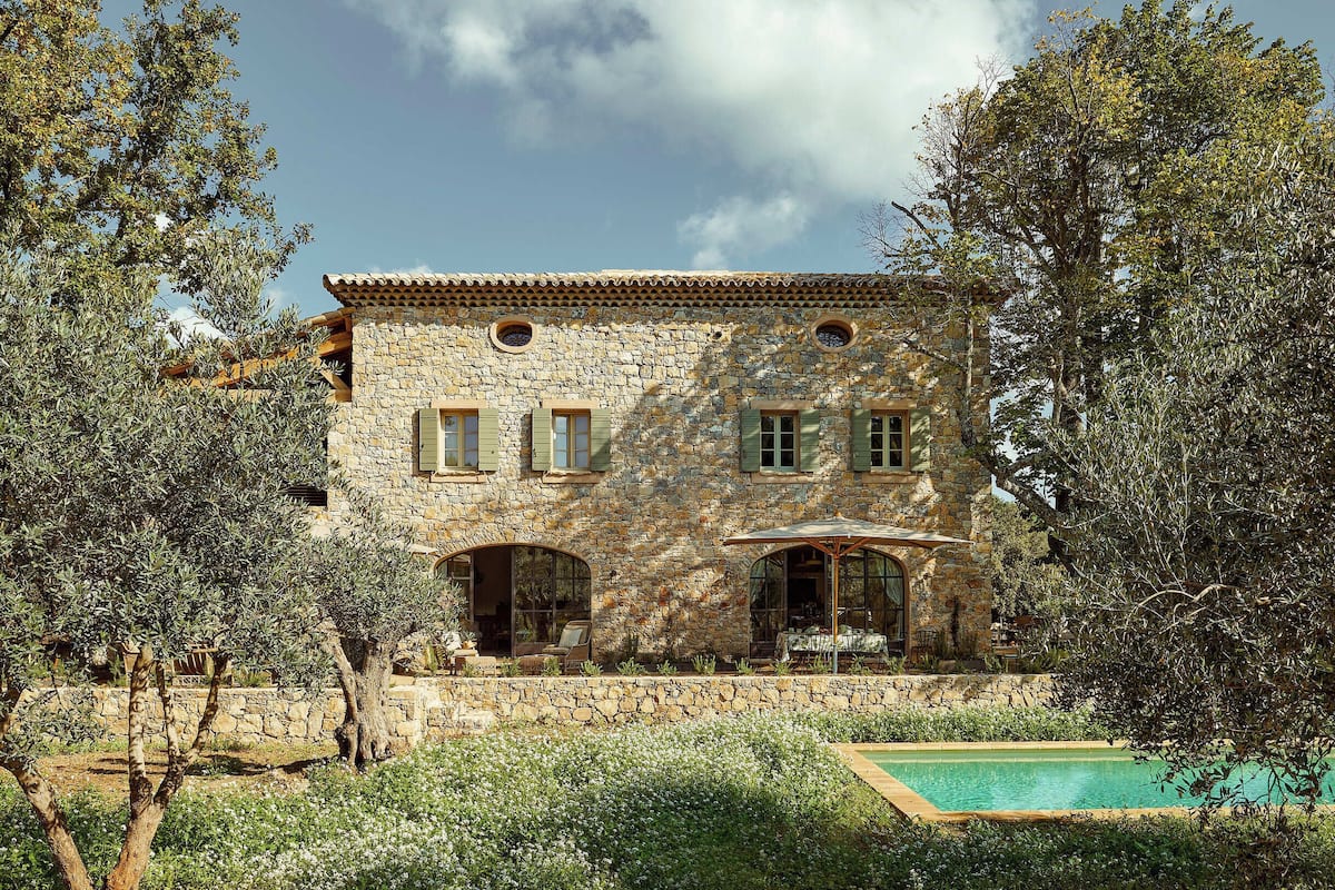 Una villa de piedra con piscina, rodeada de olivos y vegetación.