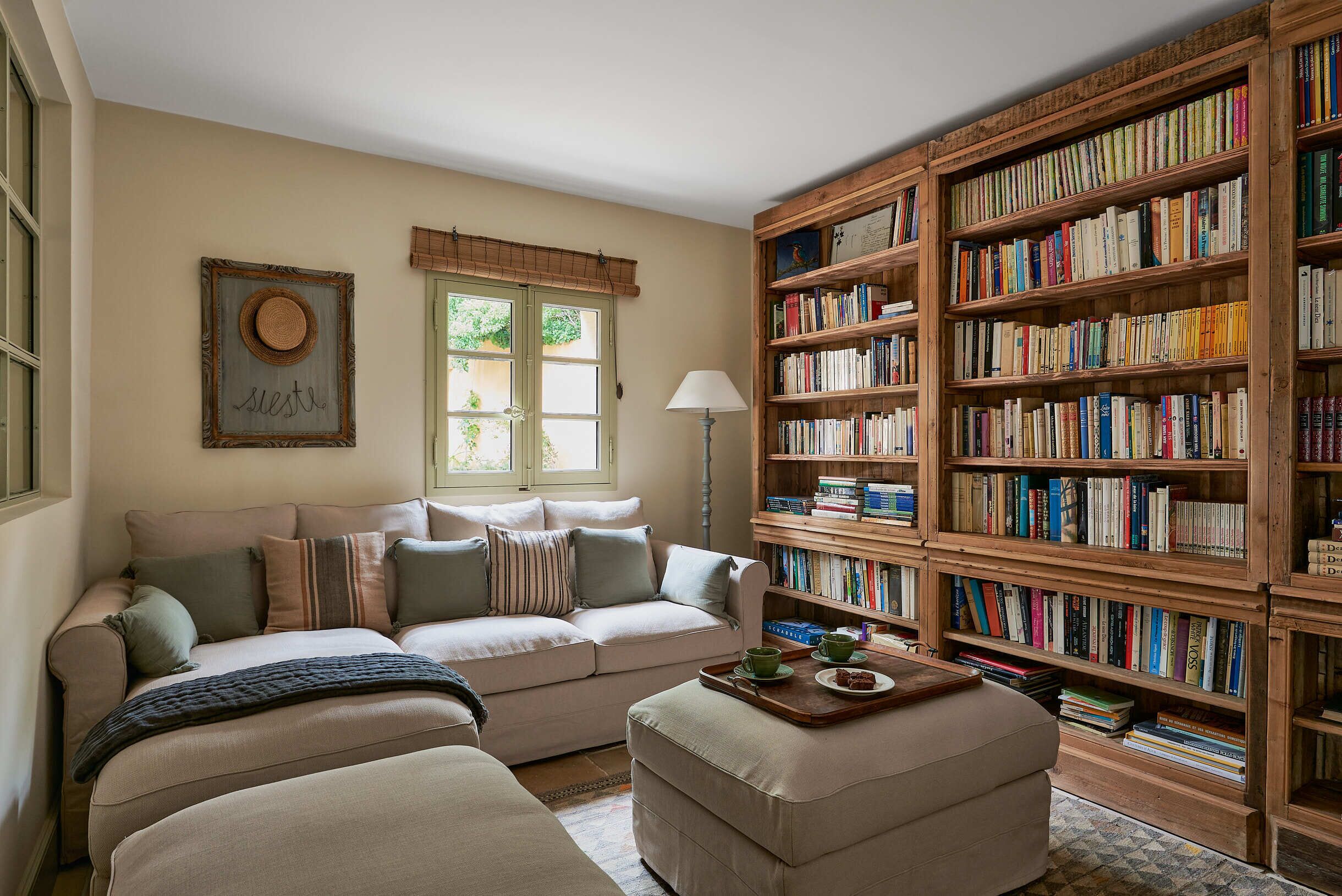 Un salón acogedor con un sofá color beige, una estantería de madera llena de libros y una ventana que ofrece vistas a zonas verdes.