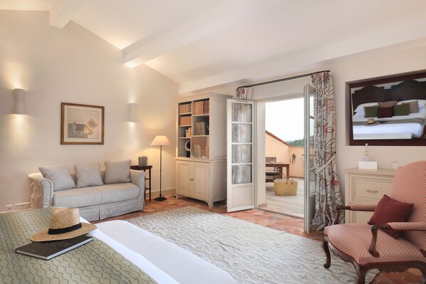 Un dormitorio acogedor con una cama, un sofá, un sillón de lectura, una estantería y un ventanal grande.
