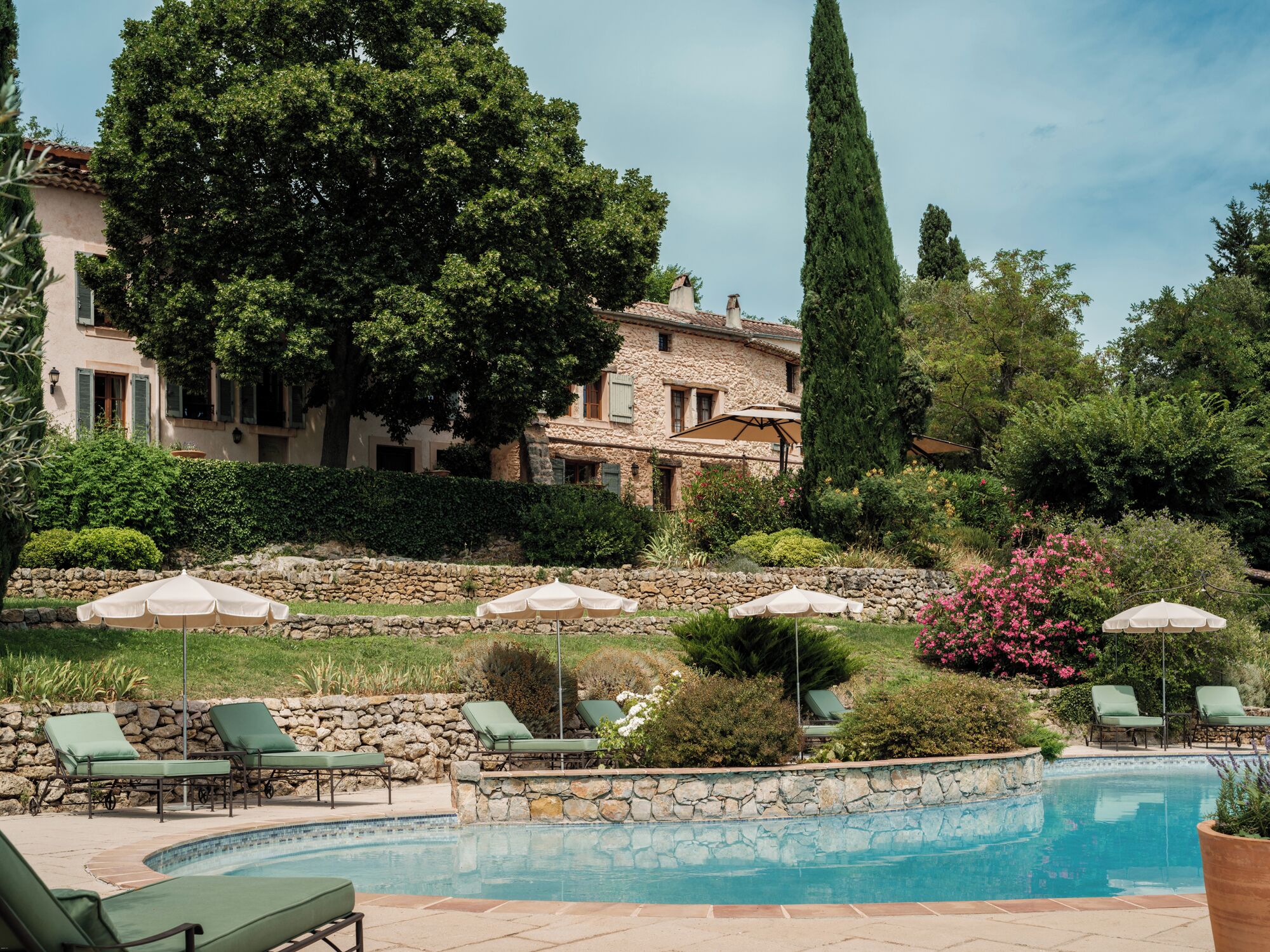 A pool area with lounge chairs and umbrellas, surrounded by stone walls and greenery.