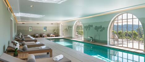 A spa area with a pool, sun loungers, and a view of the mountains.