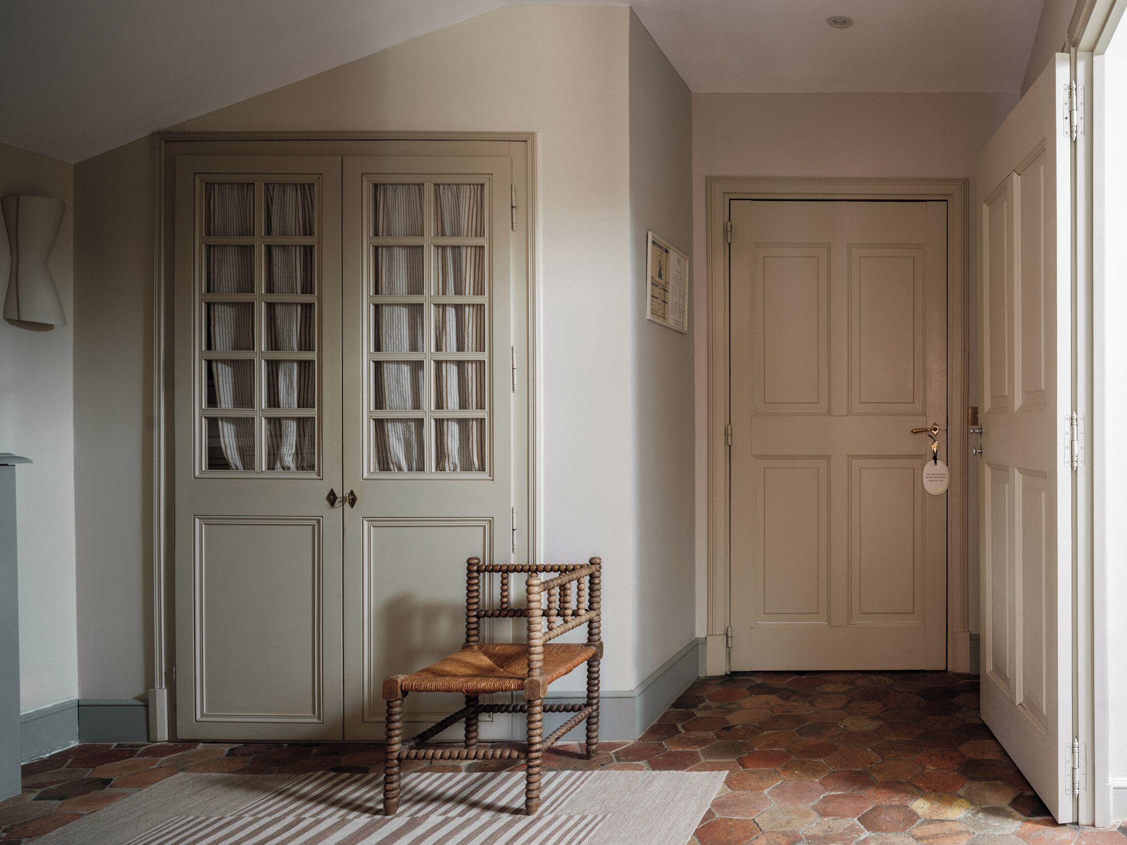 A hallway with a wooden chair, a door with a keyhole, and a patterned rug.