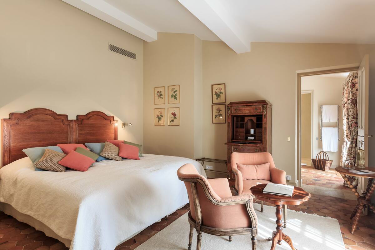 Un dormitorio con una cama grande, cabecera de madera, una silla, una mesita y un armario.