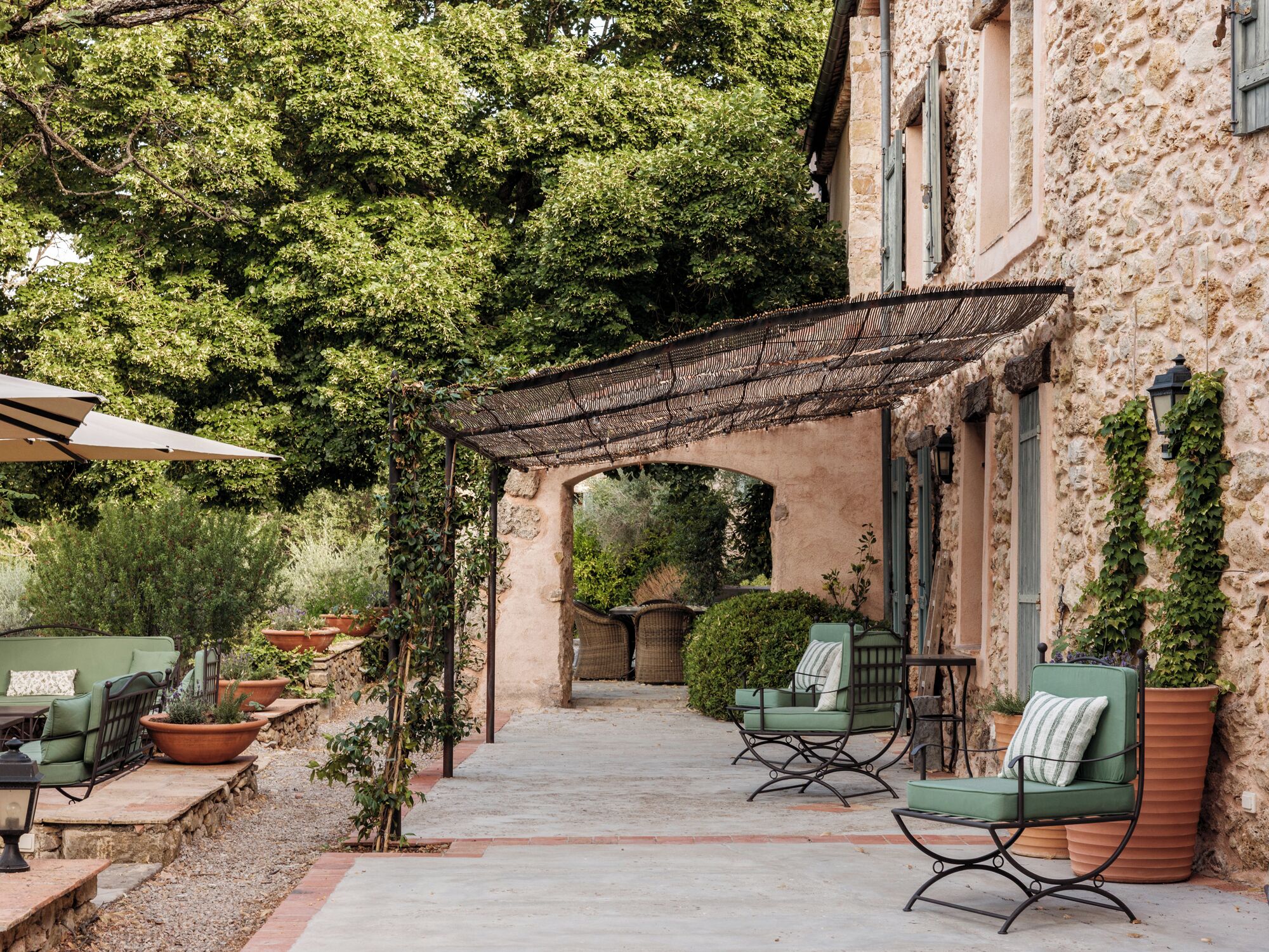 An outdoor patio with stone flooring, green cushioned chairs, and a pergola.