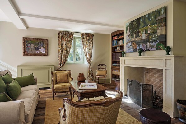 A cozy living room with a fireplace, a bookshelf, and a large painting.