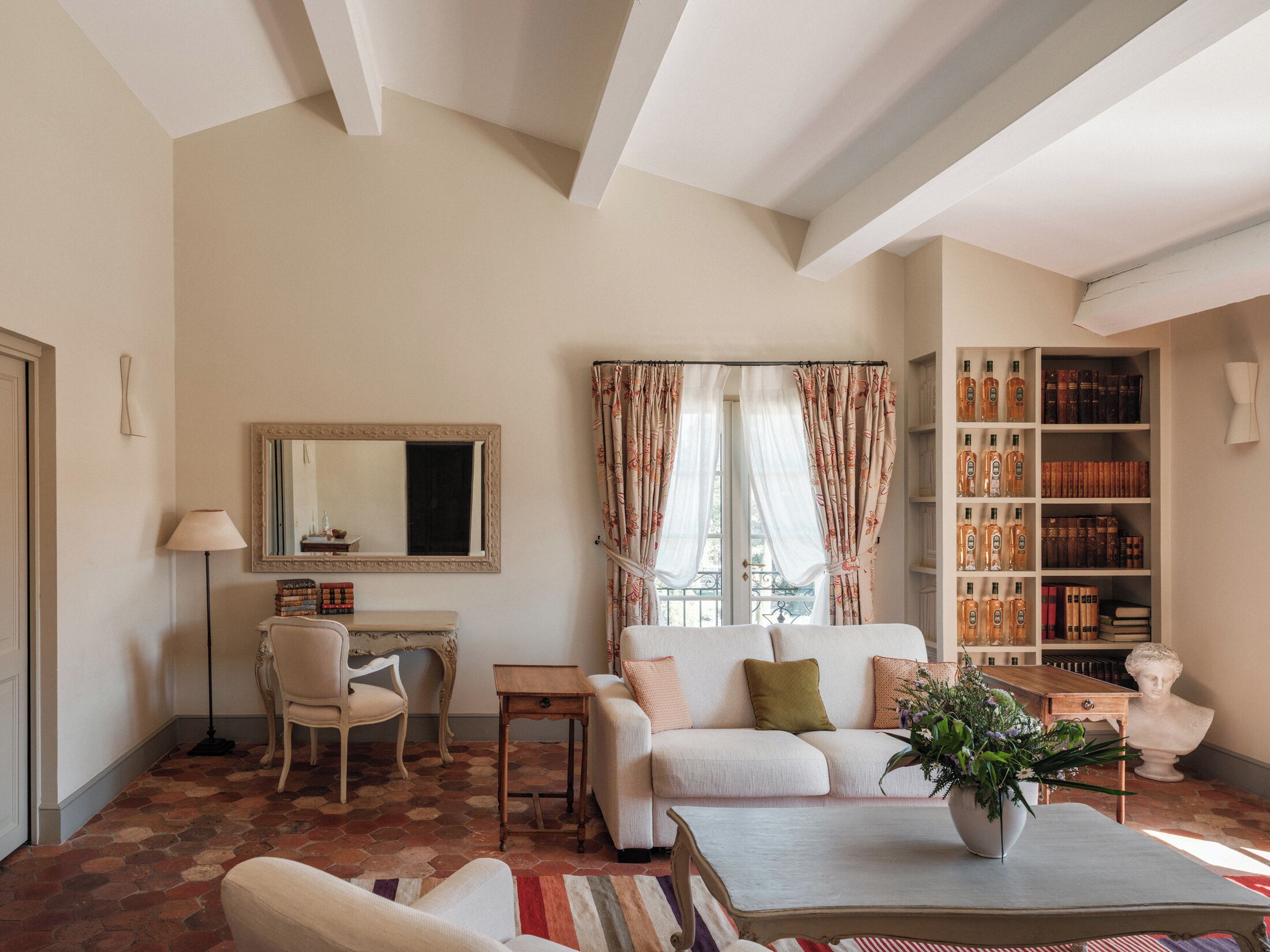 A living room with a sofa, a coffee table with a plant, a bookshelf, and a window with curtains.