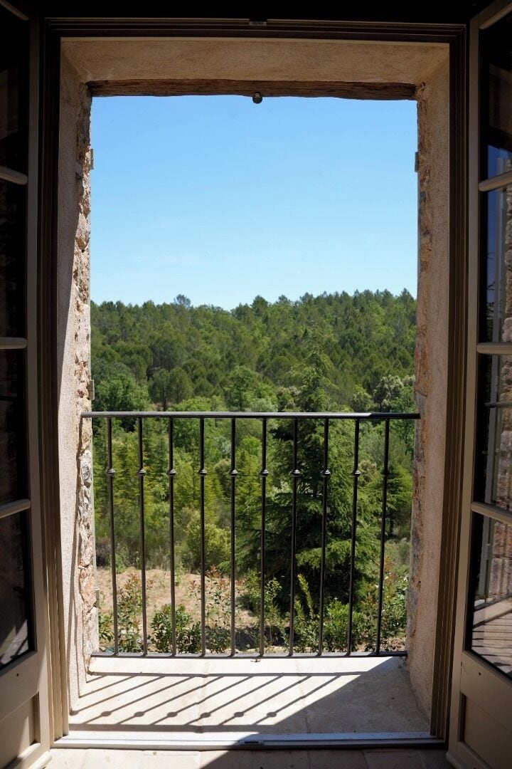 Un balcón con barandilla de metal, pared de piedra y vistas a una ladera boscosa.