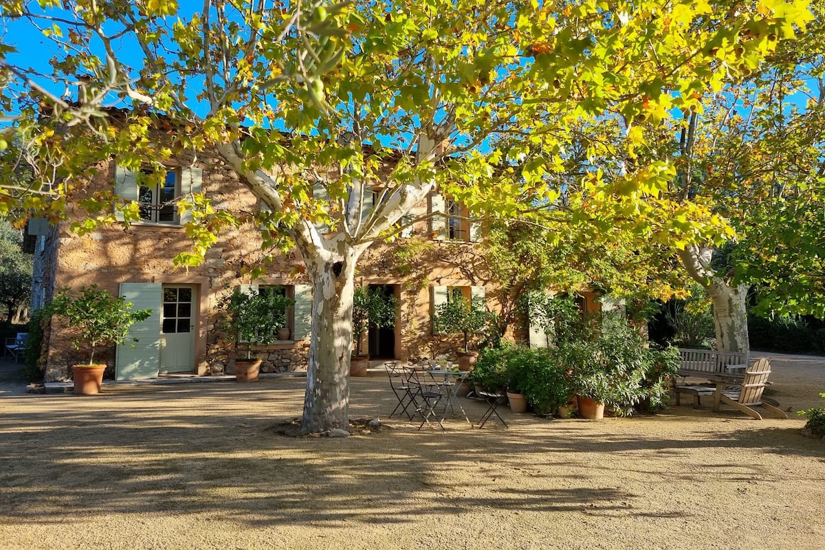 Un edificio rústico de piedra con un patio, rodeado de árboles con hojas amarillas.